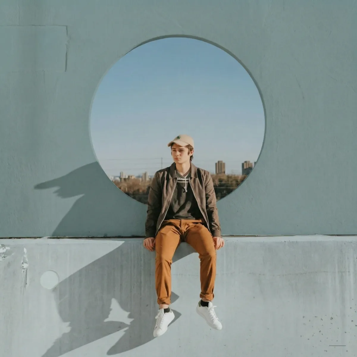 A man in a field jacket and tan trousers sitting in a round concrete window